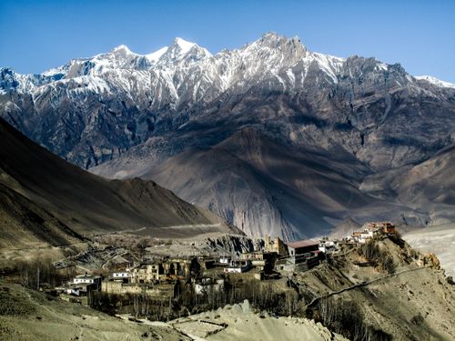 Free From above picturesque view of residential buildings surrounded by high rough ridge with snowy peaks under cloudless sky in winter Stock Photo