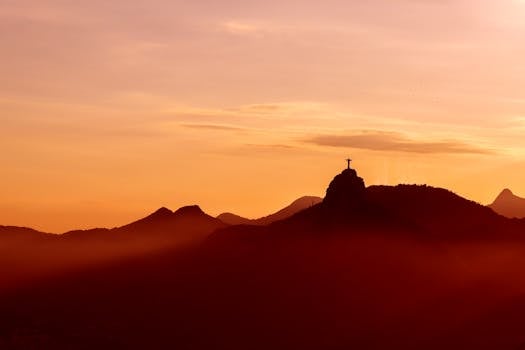 Silhouette of Christ the Redeemer statue at sunset with dramatic skies in Rio de Janeiro.