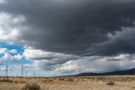 Breathtaking view of thick dark clouds on sky with lightning above uneven field with growing plants near metal towers and mountains in gloomy weather