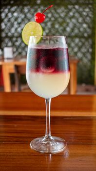 Colorful cherry-lime layered cocktail served in a chilled wine glass on a wooden table.