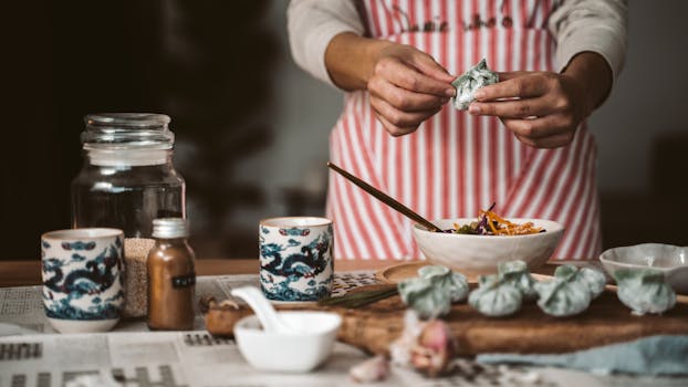 Close-up of hands making dumplings with ingredients, embodying homemade Asian cuisine.