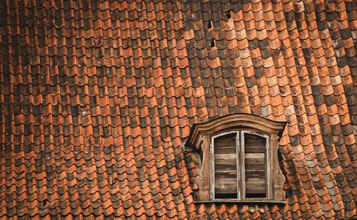 Free Tiled roof details of old fashioned building with ornamental attic window with wooden shutter Stock Photo