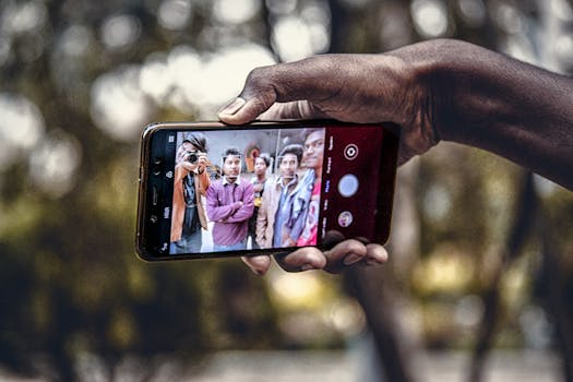 A group of friends captures a selfie outdoors using a smartphone in India. Close-up of hands holding the phone with faces in focus.