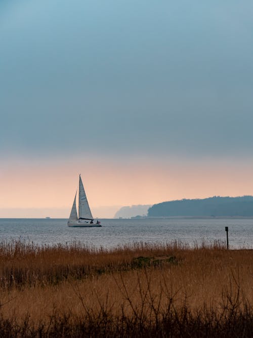 Free A Sailboat Sailing on the Sea During Sunrise Stock Photo