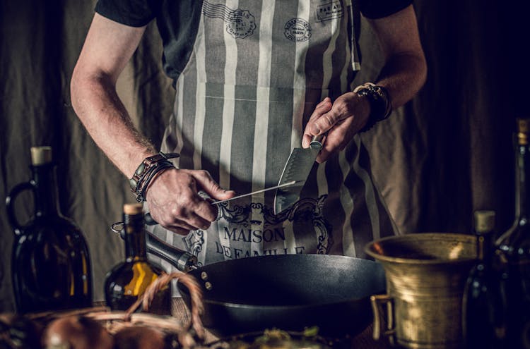 Crop Faceless Chef Sharpening Knives Before Preparing Food In Frying Pan