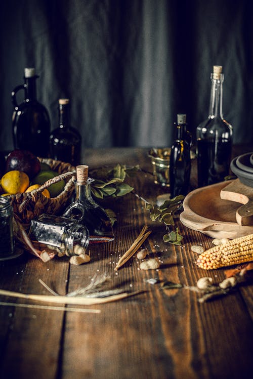 Free From above of bottles with assorted oil and vinegar placed on wooden table in kitchen near fruit basket composed with corn and herbs Stock Photo