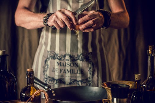 Crop unrecognizable young male chef in apron breaking egg into frying pan while cooking delicious traditional food in kitchen