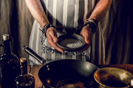 High angle of crop unrecognizable male chef adding kosher salt in pan while cooking traditional lunch in restaurant kitchen