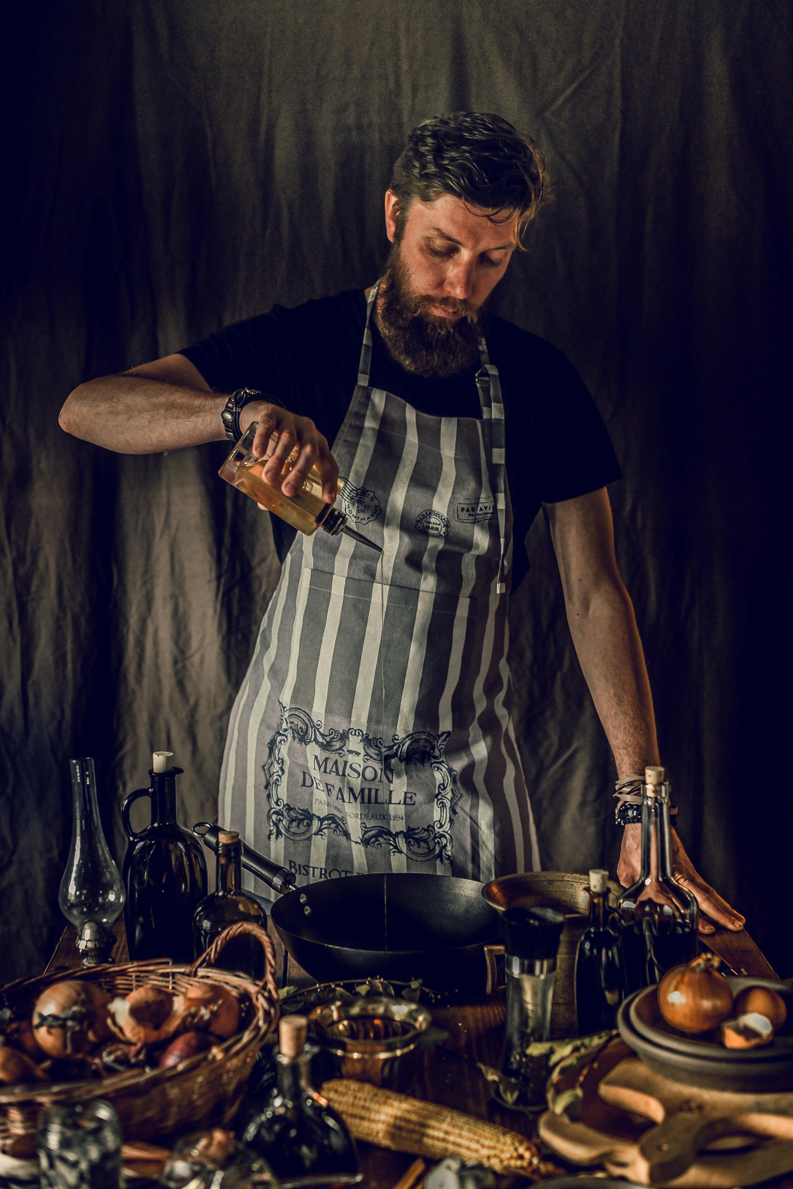 serious young male chef adding oil to dish in kitchen