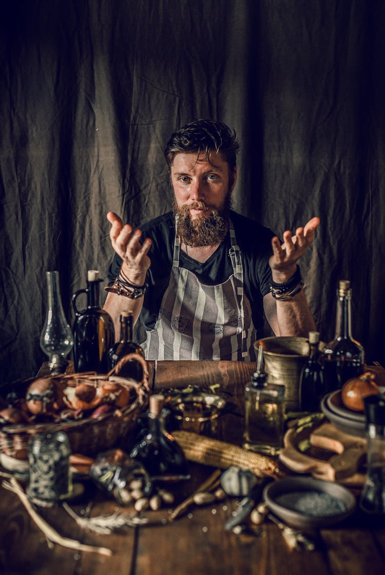 Vertical Shot Of Bearded Chef Sitting At Wooden Old Table