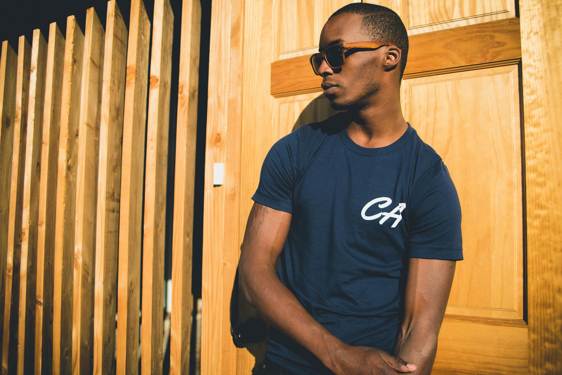 Man in Blue T-shirt Leaning Against Brown Wooden Wall