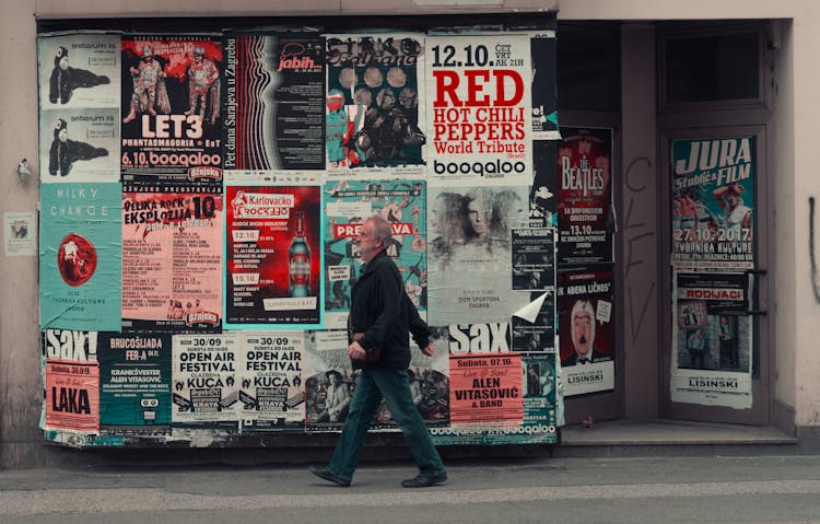 Old Man Walking Near Board With Posters On Street