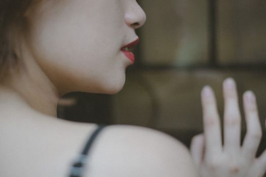 A close-up image showcasing a woman with striking red lips and a delicate pose, emphasizing elegance and mystery.