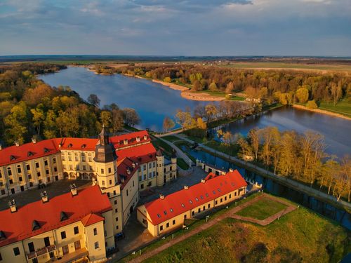 Free Drone view scenery of beige Nesvizh Castle with brown tiled roofs located on green riverside in Belarus Stock Photo