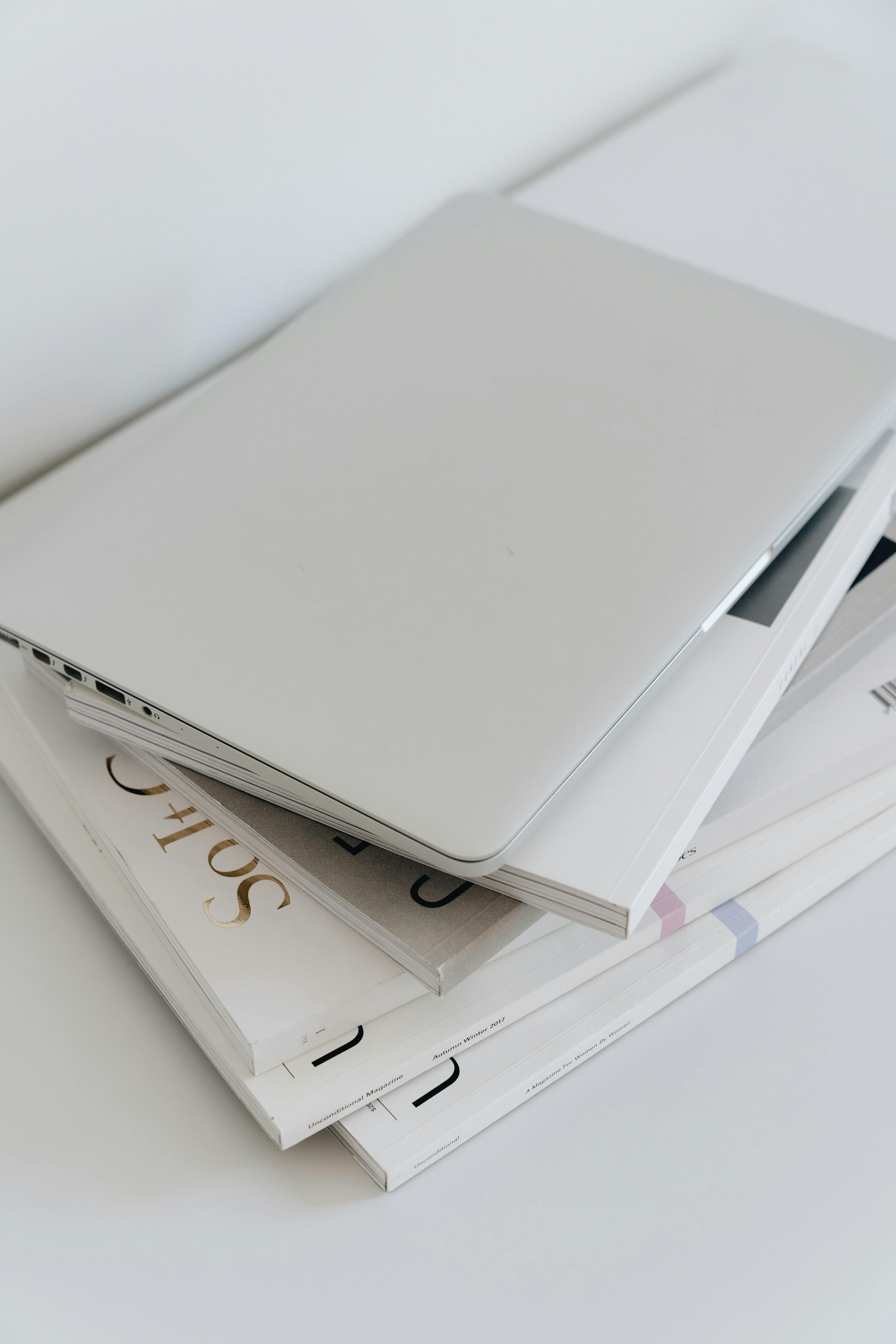 A minimalist still life composition featuring a closed laptop on top of a stack of books.