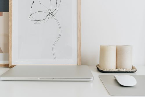 Free A minimalist home office setup with a closed laptop, framed artwork, and candles on a white desk. Stock Photo