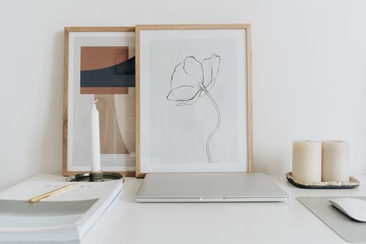 Elegant minimalist home office desk setup with framed art, candles, and a closed laptop.