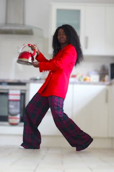 Chic woman in red outfit holding a kettle in modern kitchen.