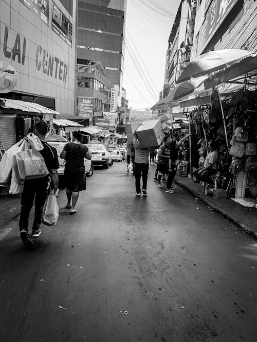 Free Black and white busy street of local market with vendors on sidewalks and people with purchases on road Stock Photo