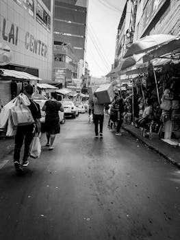Black and white busy street of local market with vendors on sidewalks and people with purchases on road