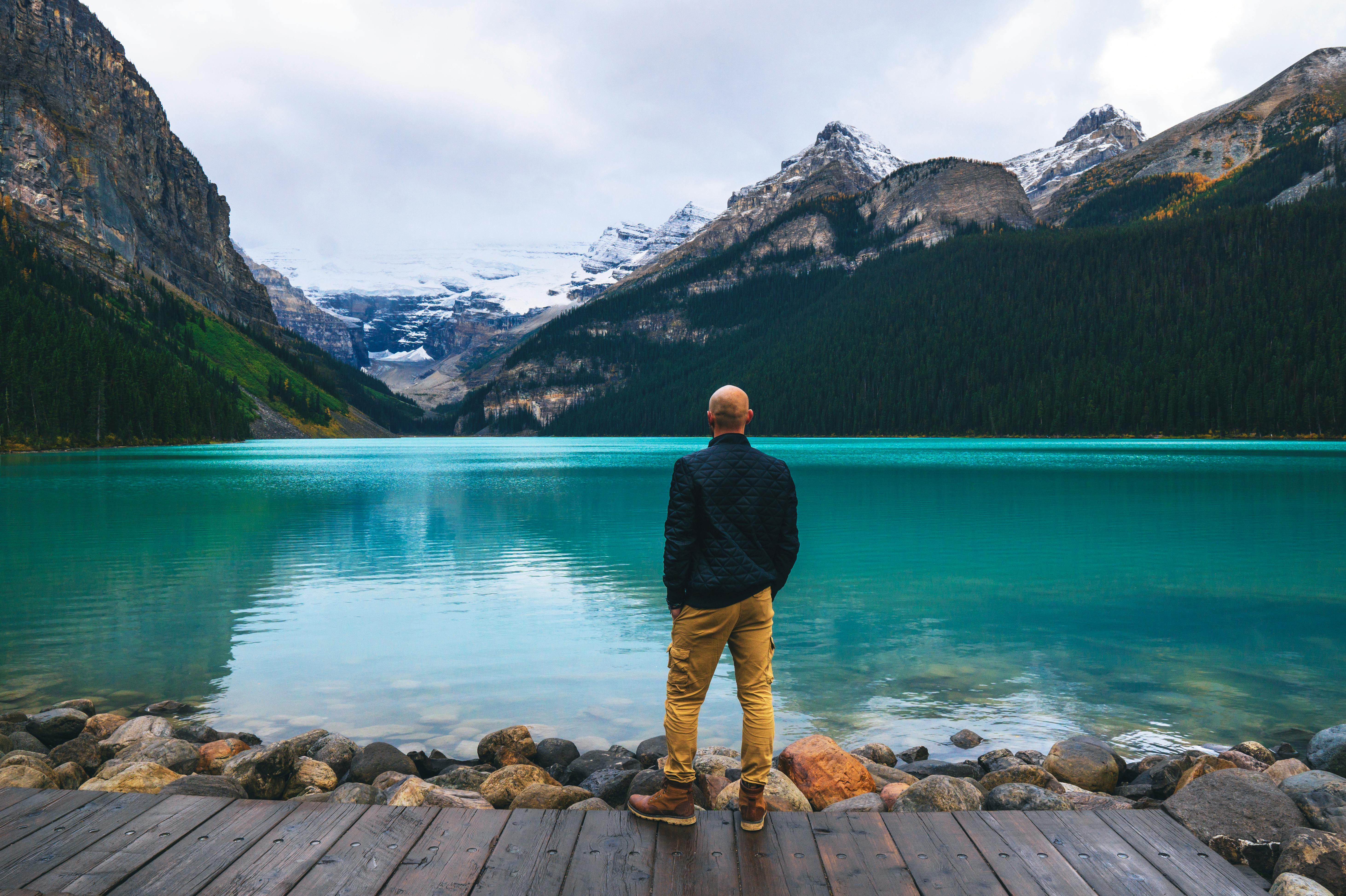 man in blue long sleeve shirt and brown pants standing on brown wooden dock