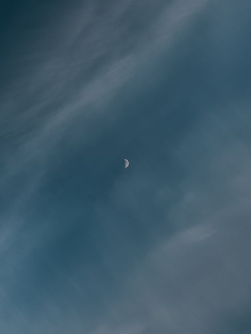 A serene blue sky featuring a prominent half moon surrounded by soft clouds.