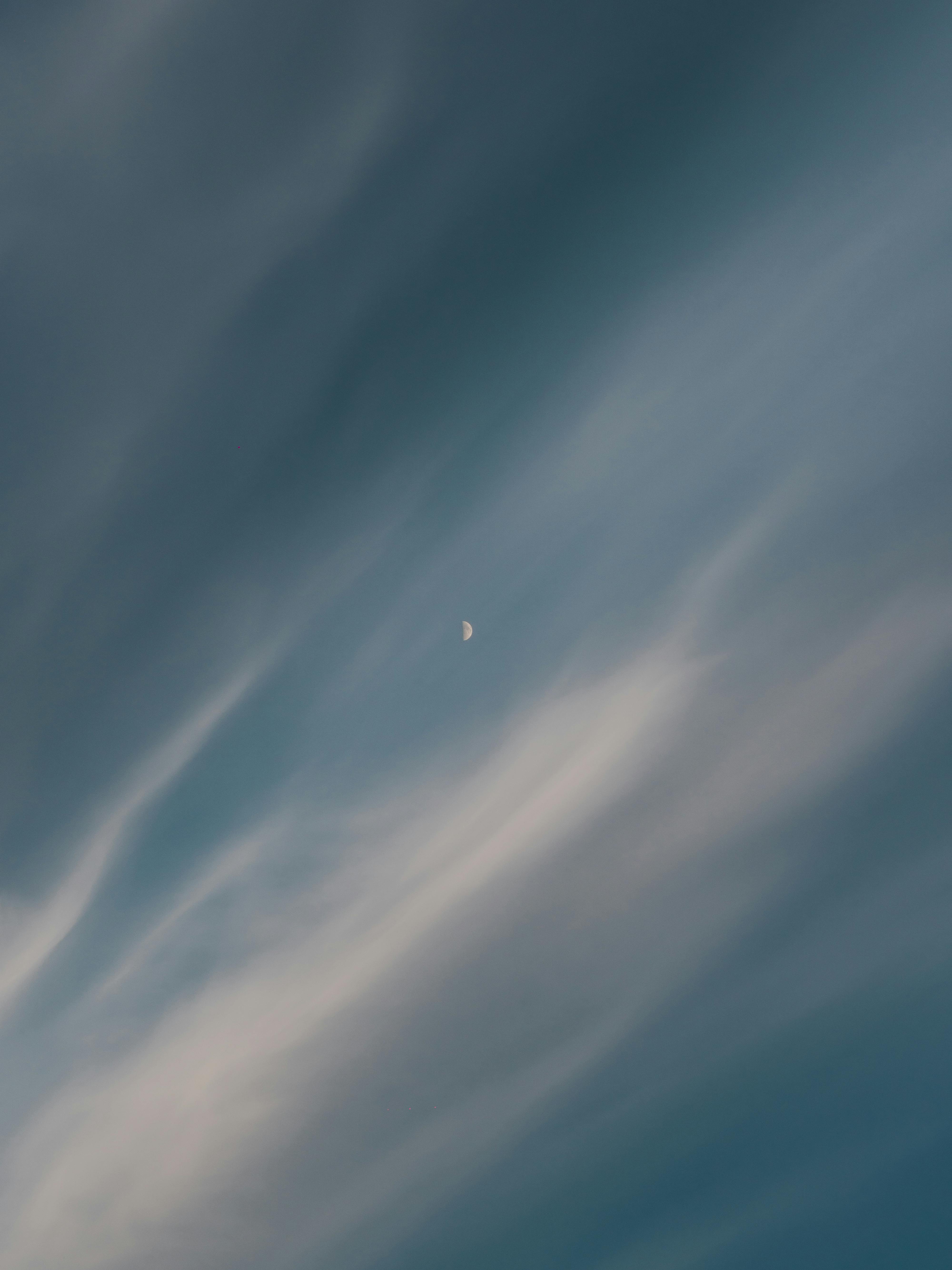 A tranquil sky featuring wispy cirrus clouds and a visible half moon, perfect for backgrounds.
