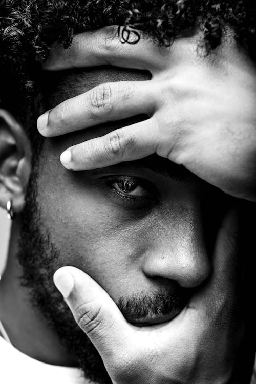 Black and white African American male with curly hair covering face with hands and looking at camera