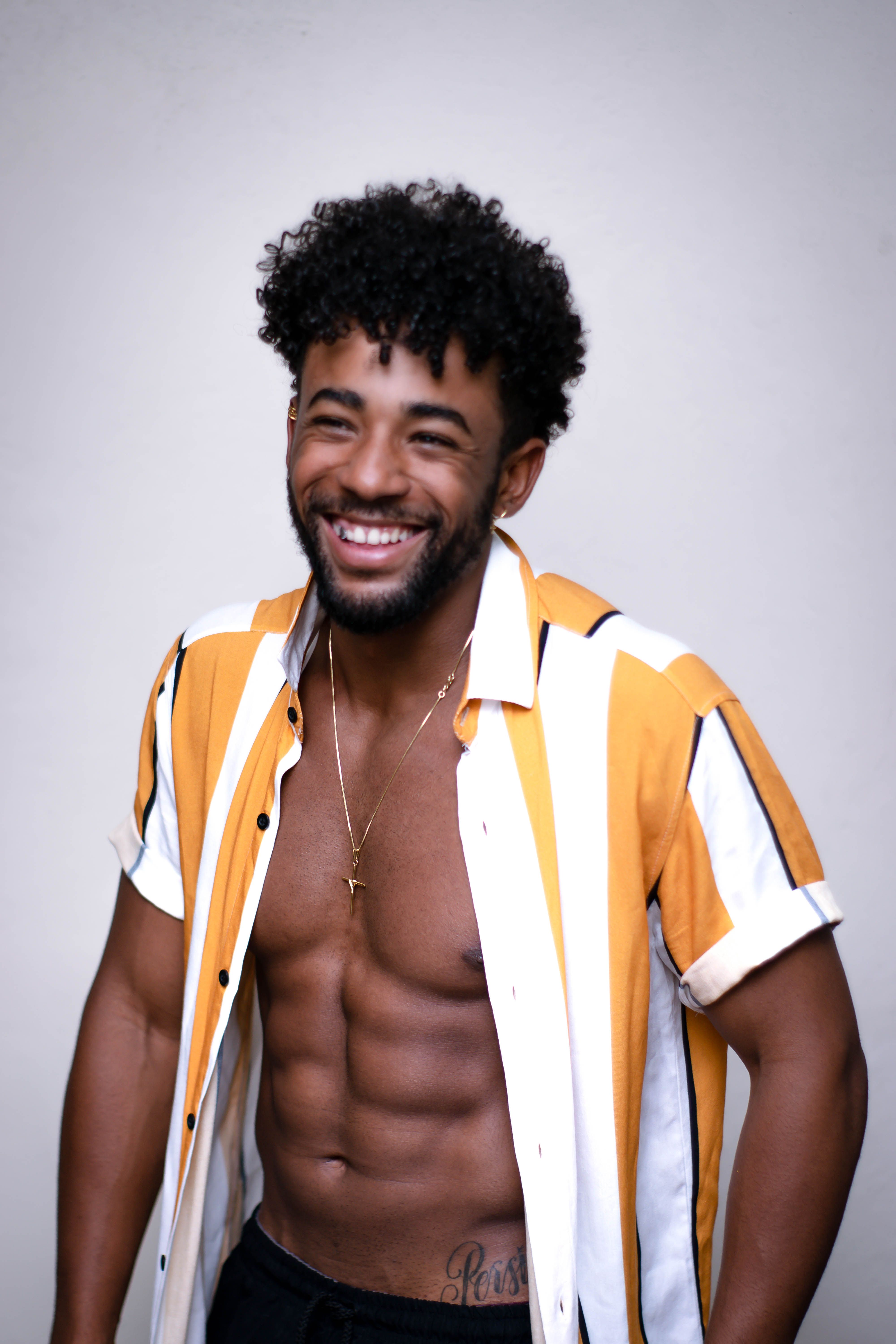 Happy African American man in unbuttoned shirt laughing brightly at camera against plain wall