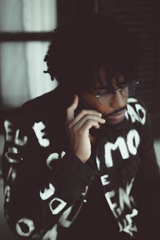A fashionable man with an afro hairstyle speaks on the phone, exuding confidence and modern style.