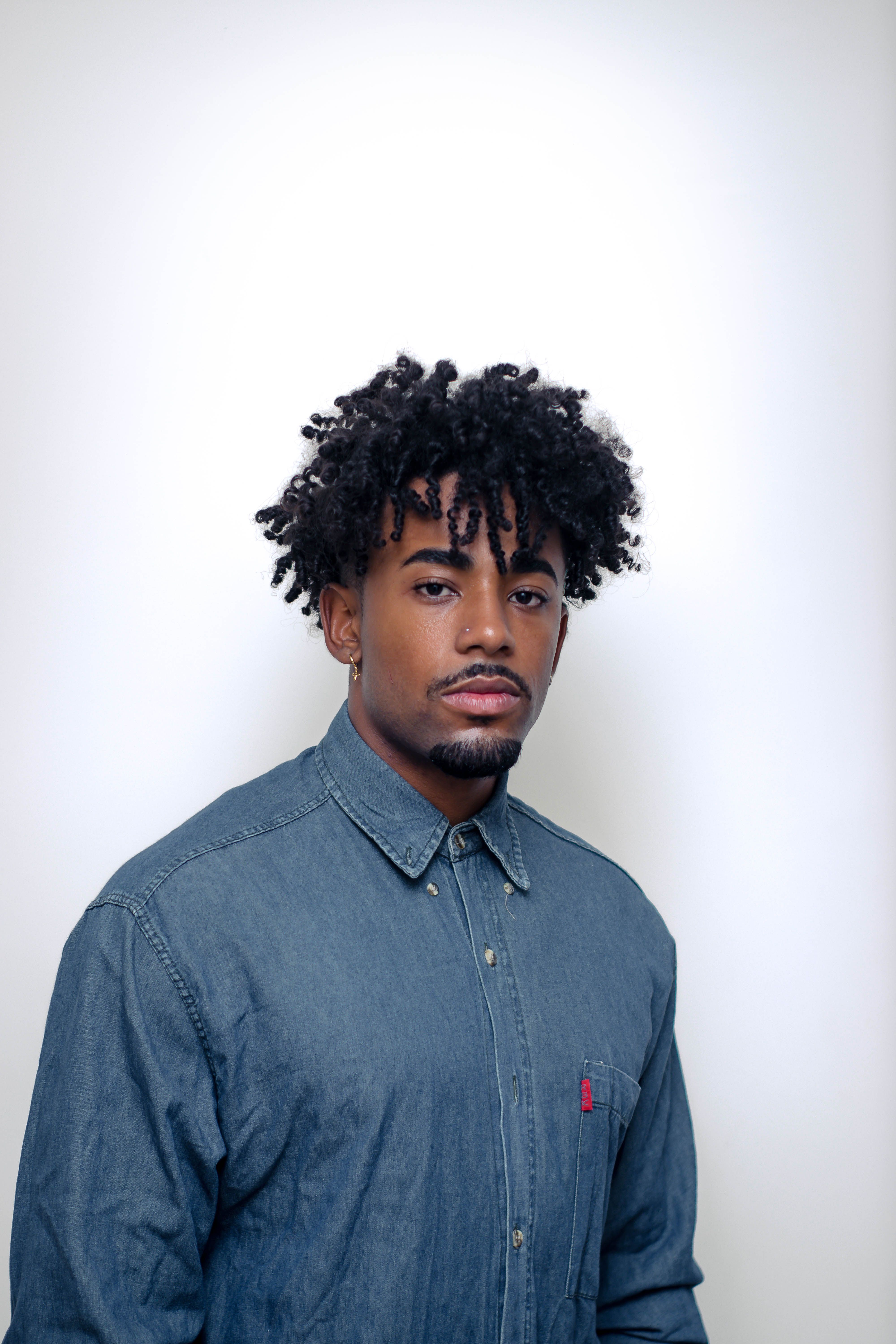 Casual young African American man with curly hair wearing bandana and denim shirt looking at camera