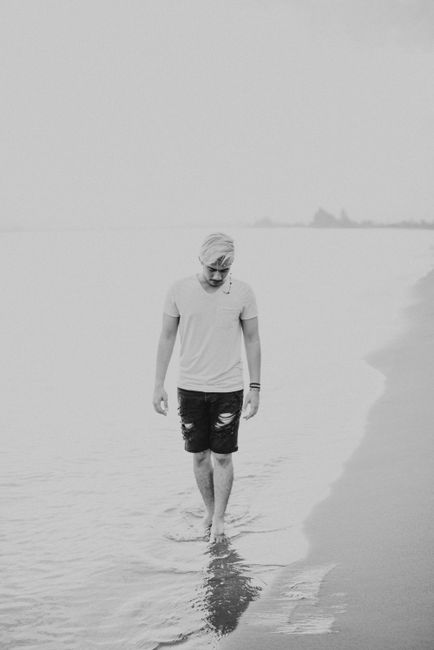 Black and white full body pensive man walking in shallow water of sea along coastline