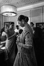 Black and white side view of young ethnic female in embroidered clothes and earring with wristbands looking down near group of people