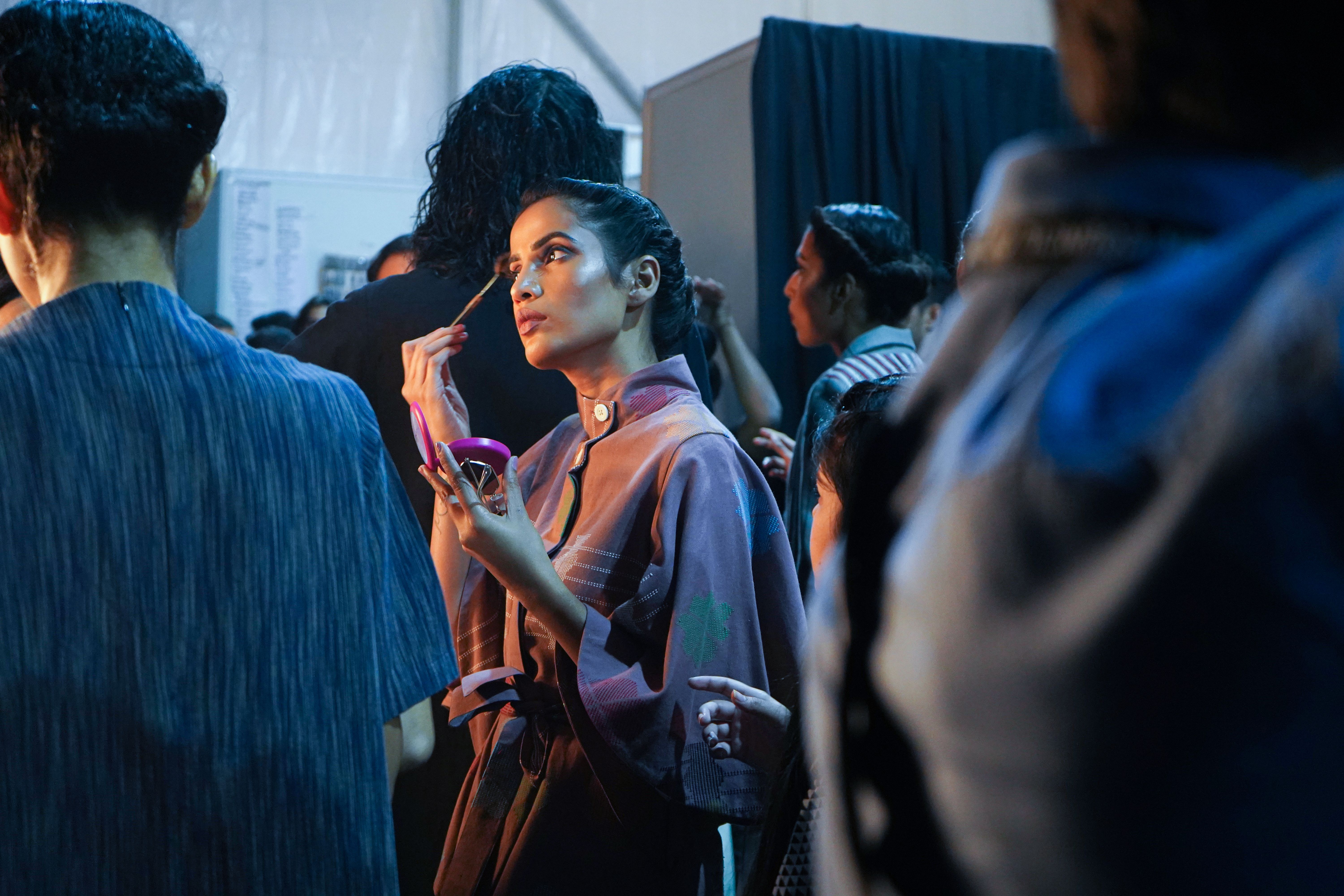 Makeup artist applying foundation under bright backstage lighting at a fashion show