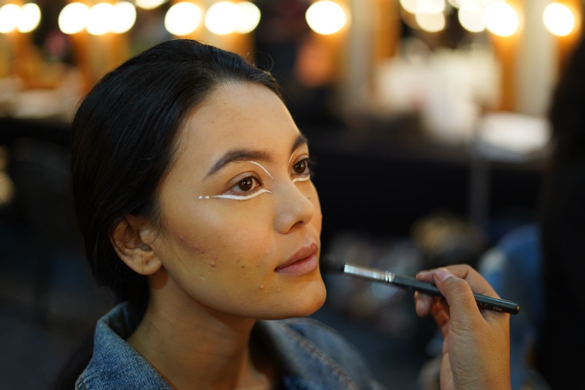 Side view of makeup artist doing makeup to young Asian female in beauty salon