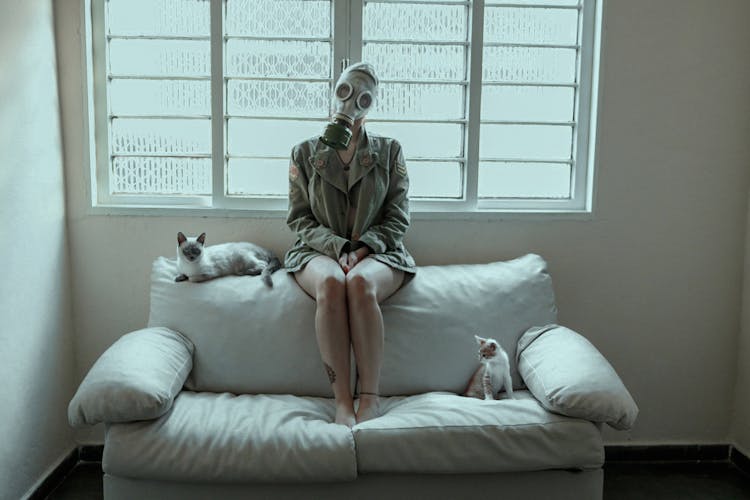 Woman Wearing Gas Mask While Sitting White Couch With Her Cats