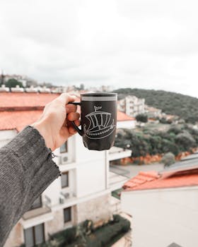 A hand holding a mug with a cityscape background, showcasing urban lifestyle.
