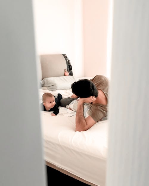 Anonymous father looking after baby on bed in apartment