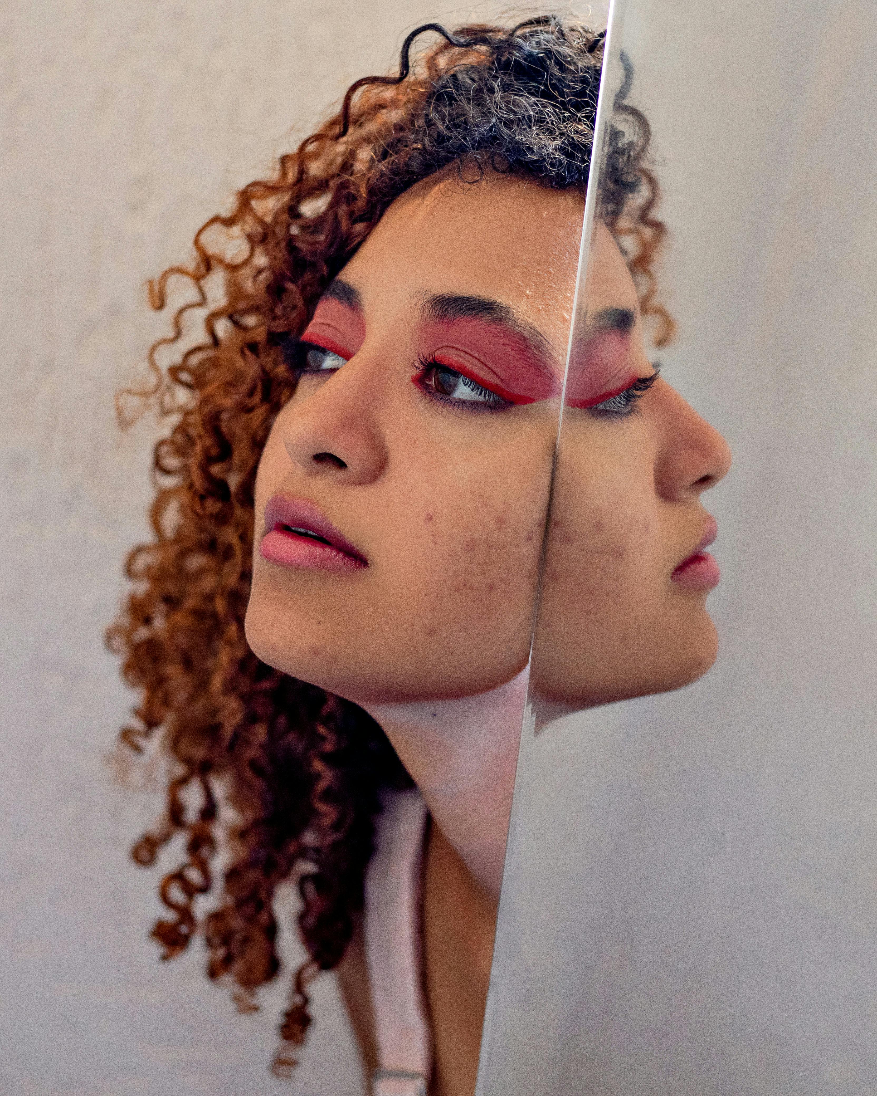 Side view of young dreamy African American female with bright makeup on eyes and lips reflecting in mirror at home while looking away