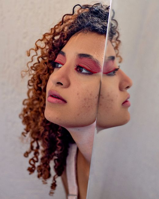 Side view of young dreamy African American female with bright makeup on eyes and lips reflecting in mirror at home while looking away