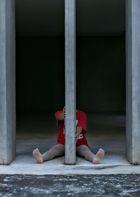 A child in a red shirt playfully sits behind a concrete column, depicting a unique architectural portrait.