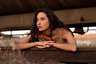 Charming young brunette lying on metal rail tracks under tank car and looking away attentively