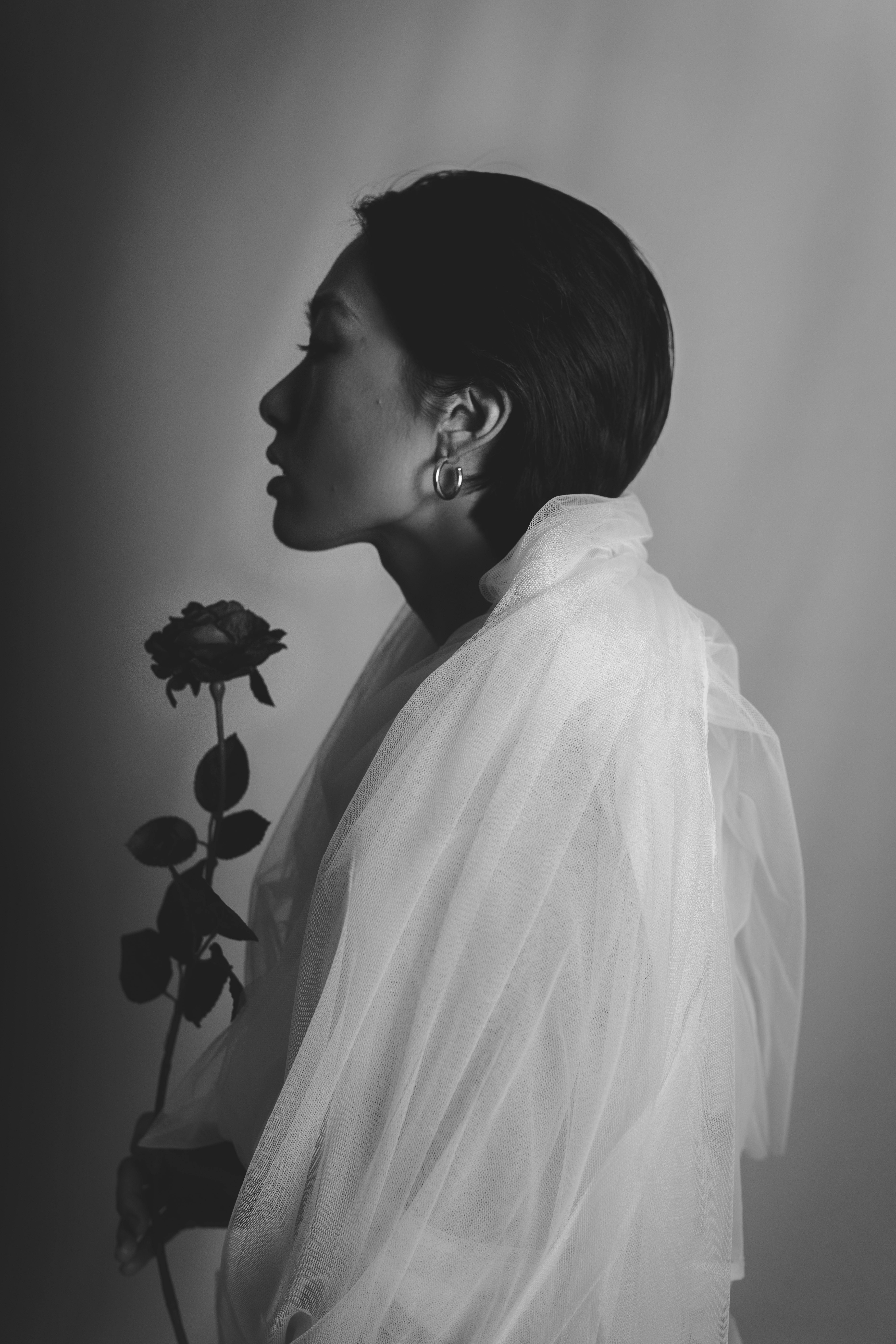 一幅优雅的黑白肖像中，一位手持玫瑰花的女子，散发着优雅与神秘