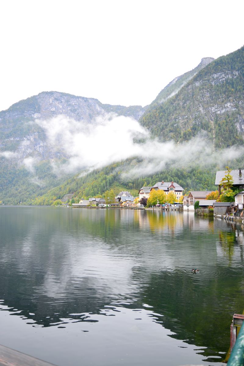 Hallstatt în toamnă cu frunzișul colorat reflectat în lacul alpin și munți cu ceață