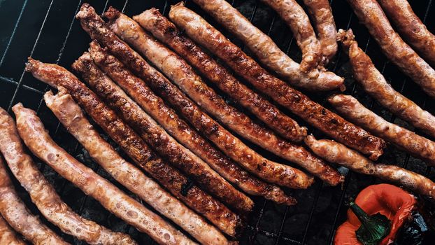 Top view appetizing pork sausages frying on hot barbecue grill near ripe capsicum