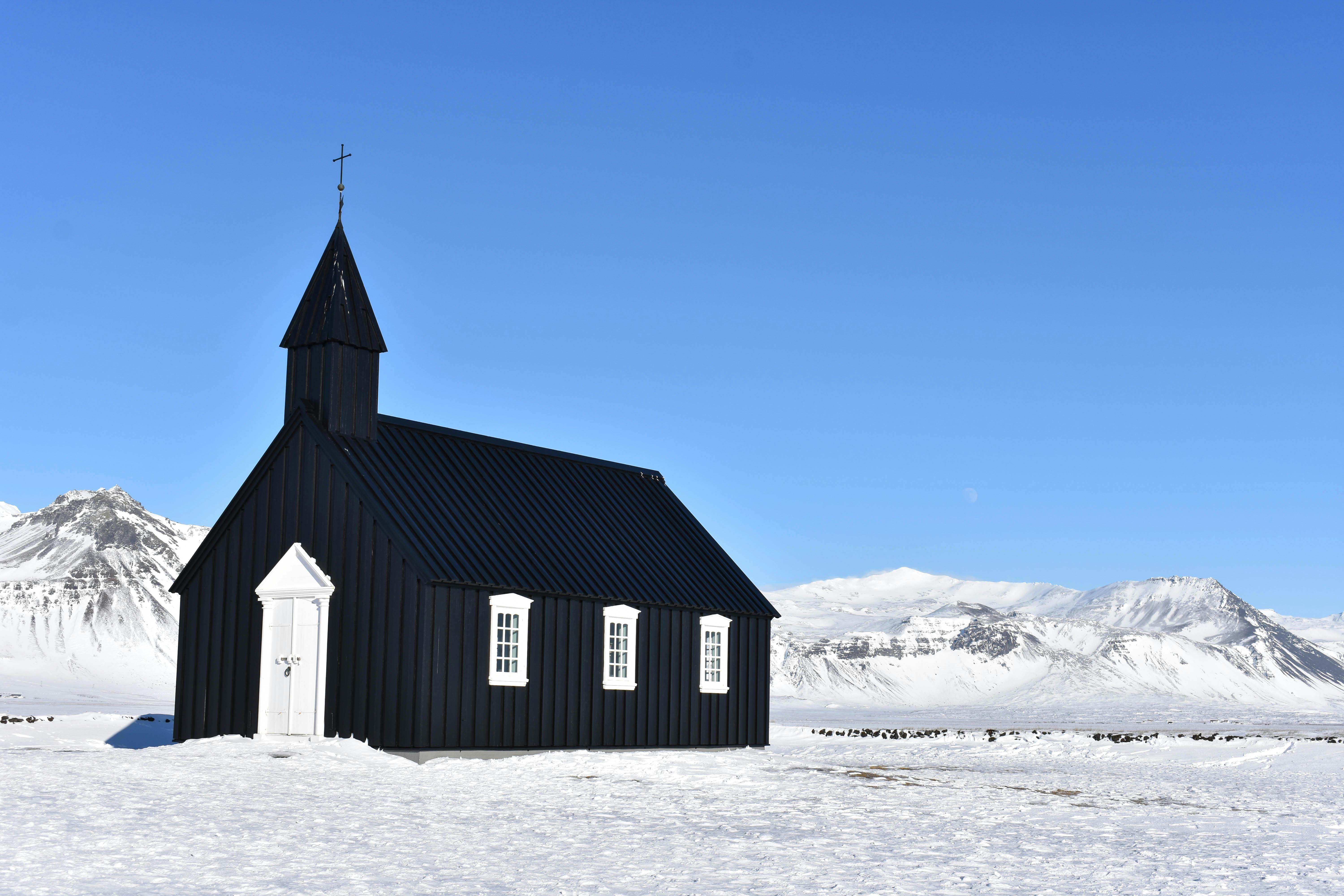 Capture of a black church in snow-covered Icelandic landscape with clear blue skies and mountains. - Reikiavik