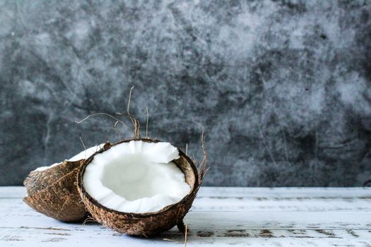 A detailed view of a halved coconut placed on a textured wooden surface.