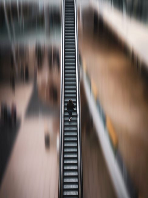 Blurred top view of a lone woman on an escalator, creating a dynamic effect in a modern indoor setting.