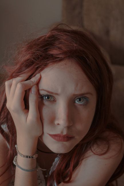 Portrait of a young woman with red hair indoors looking pensive.