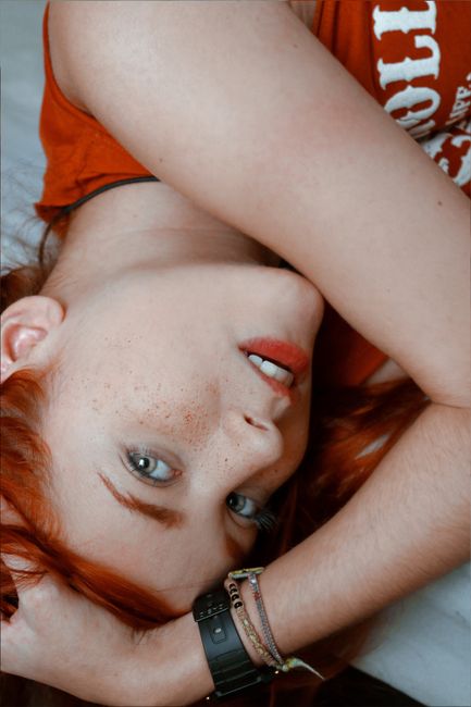 Artistic portrait of a freckled redhead woman lying indoors, showcasing unique beauty and style.